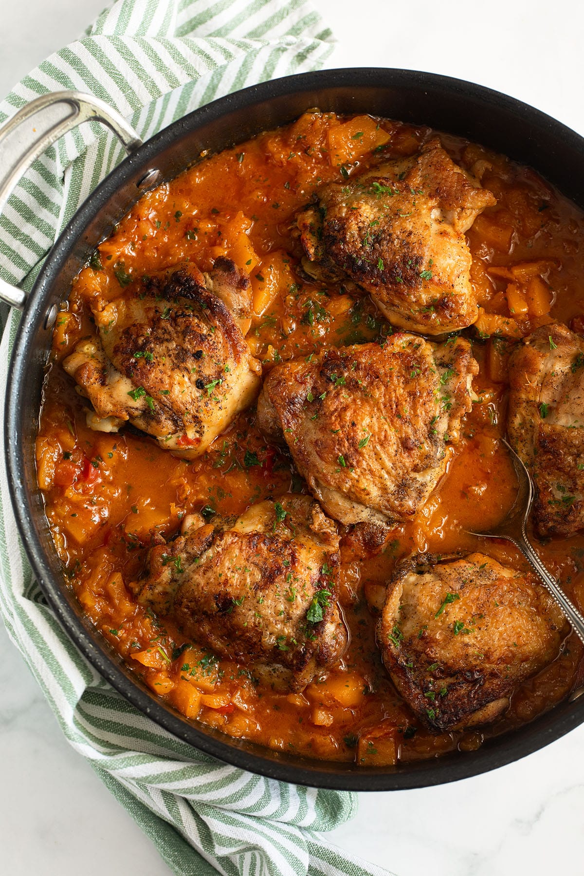 six crispy chicken thighs in butternut squash sauce in a large pan.