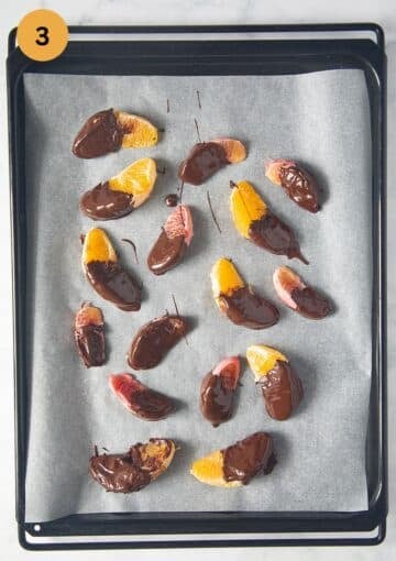 orange slices halfway dipped in melted chocolate setting on a lined baking sheet.