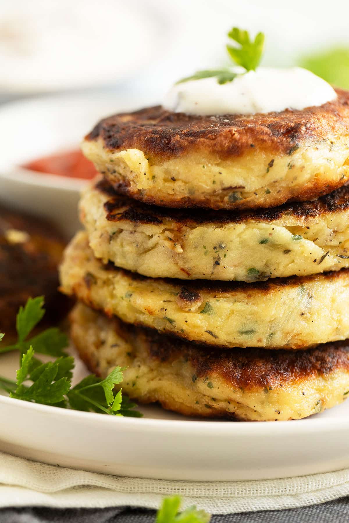 four thick and crispy mashed potato cakes stapled on a plate and garnished with sour cream.