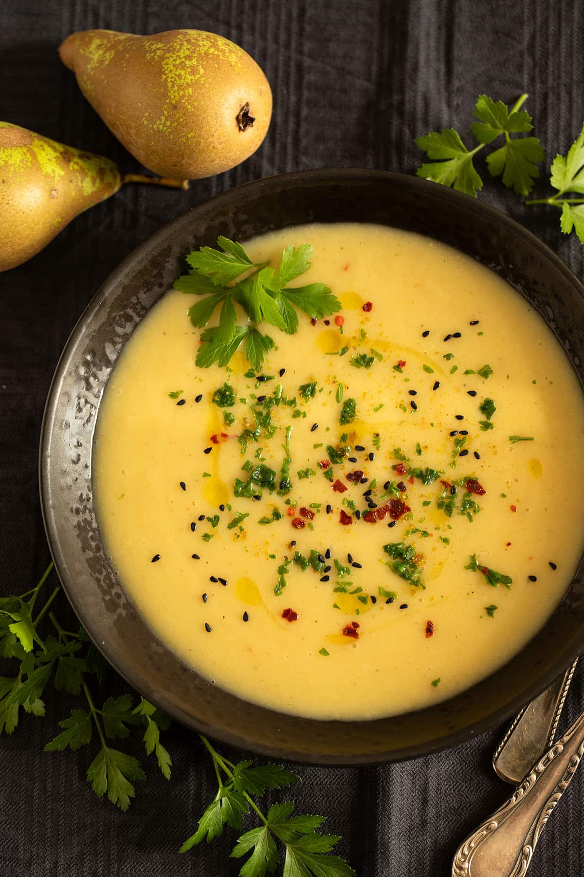 parsnip and potato soup sprinkled with herbs in a bowl, two pears beside it.