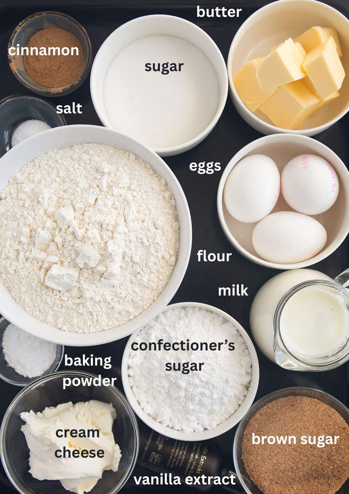labeled ingredients for making swirl cake with cinnamon, flour, eggs. butter, cream cheese, brown sugar, milk, sugar.