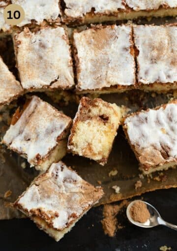 squares of cinnamon swirl cake cut on a piece of parchment paper and a teaspoon full of cinnamon beside it.