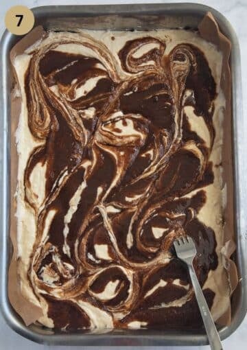 swirling cinnamon topping through cake batter using a spoon in a large baking dish.