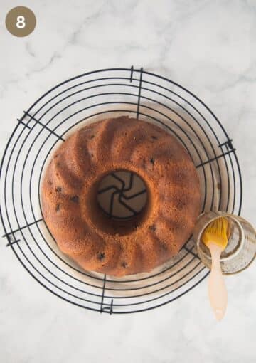 baked bundt irish cake on a wire rack with a small glass with glazing and a brush.