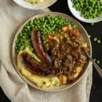 irish bangers and mash served with peas on a plate.