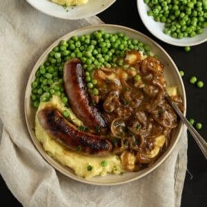 irish bangers and mash served with peas on a plate.
