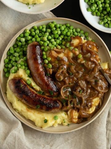 irish bangers and mash served with peas on a plate.