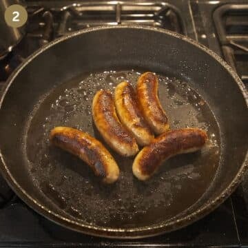 five sausages frying in a nonstick pan.