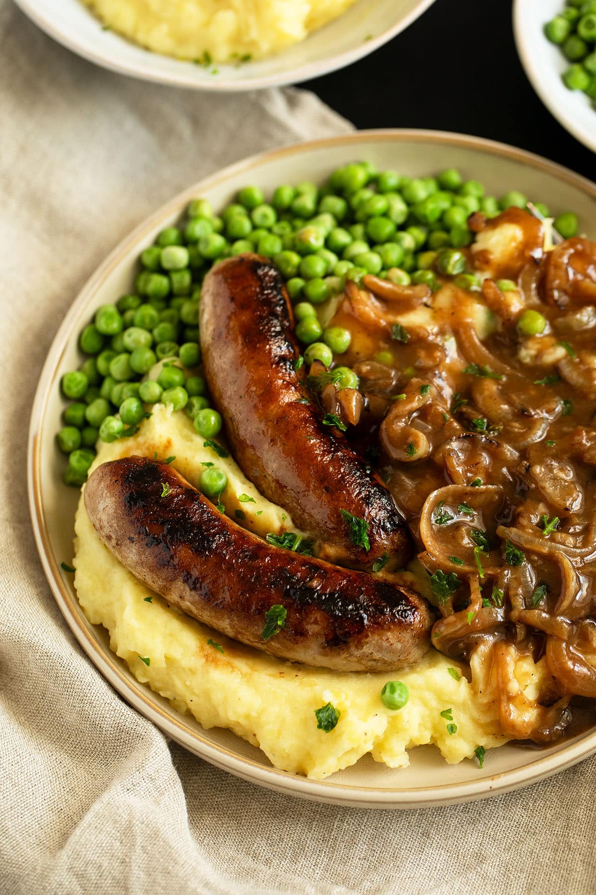 two irish bangers and mashed potatoes with peas on a large plate.