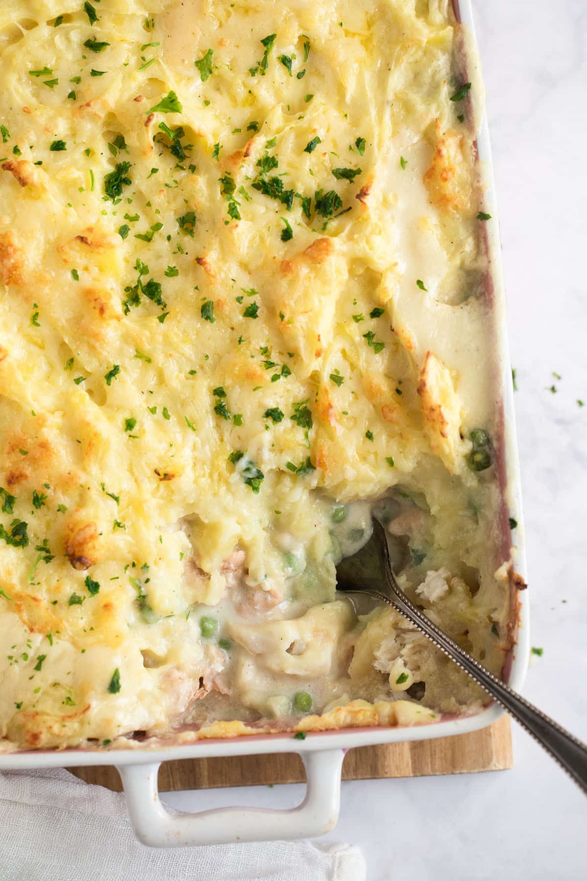 fish pie with salmon, cod and mashed potatoes in a baking dish with a spoon in it.
