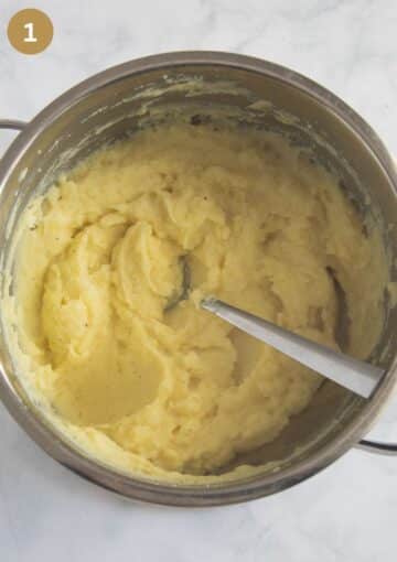 creamy mashed potatoes for making fish pie in a pot with a spoon in it.