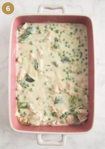 fish pie filling with peas and leeks in white sauce in a baking dish.