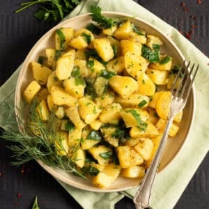 smothered potatoes with green onions, a sprig of dill and a fork on a plate.