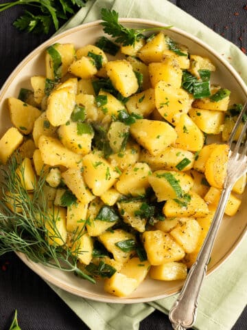smothered potatoes with green onions, a sprig of dill and a fork on a plate.