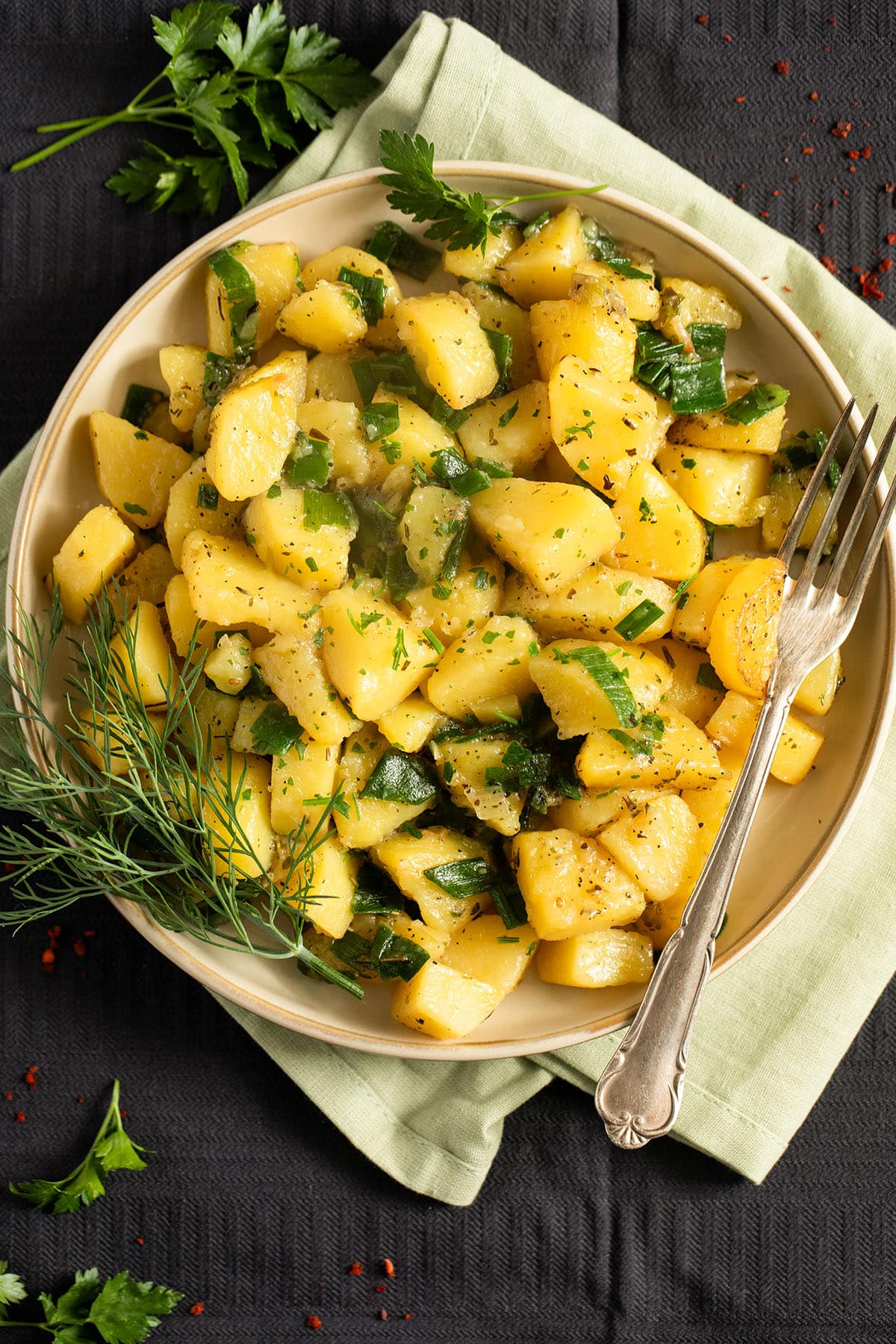 a plate of potatoes with green onions and a fork.