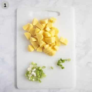 potato cubes and chopped green onions on a cutting board.
