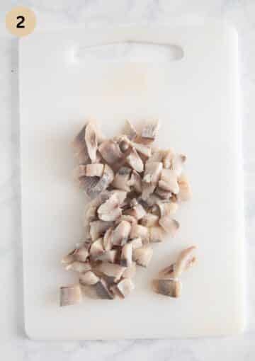 chopped pickled herring for making salad on a cutting board.