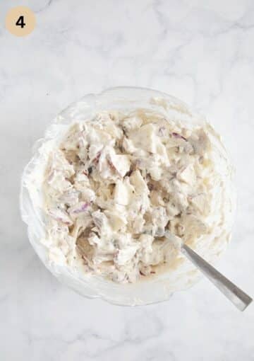 mixing herring salad with onions, apples and sour cream in a bowl.