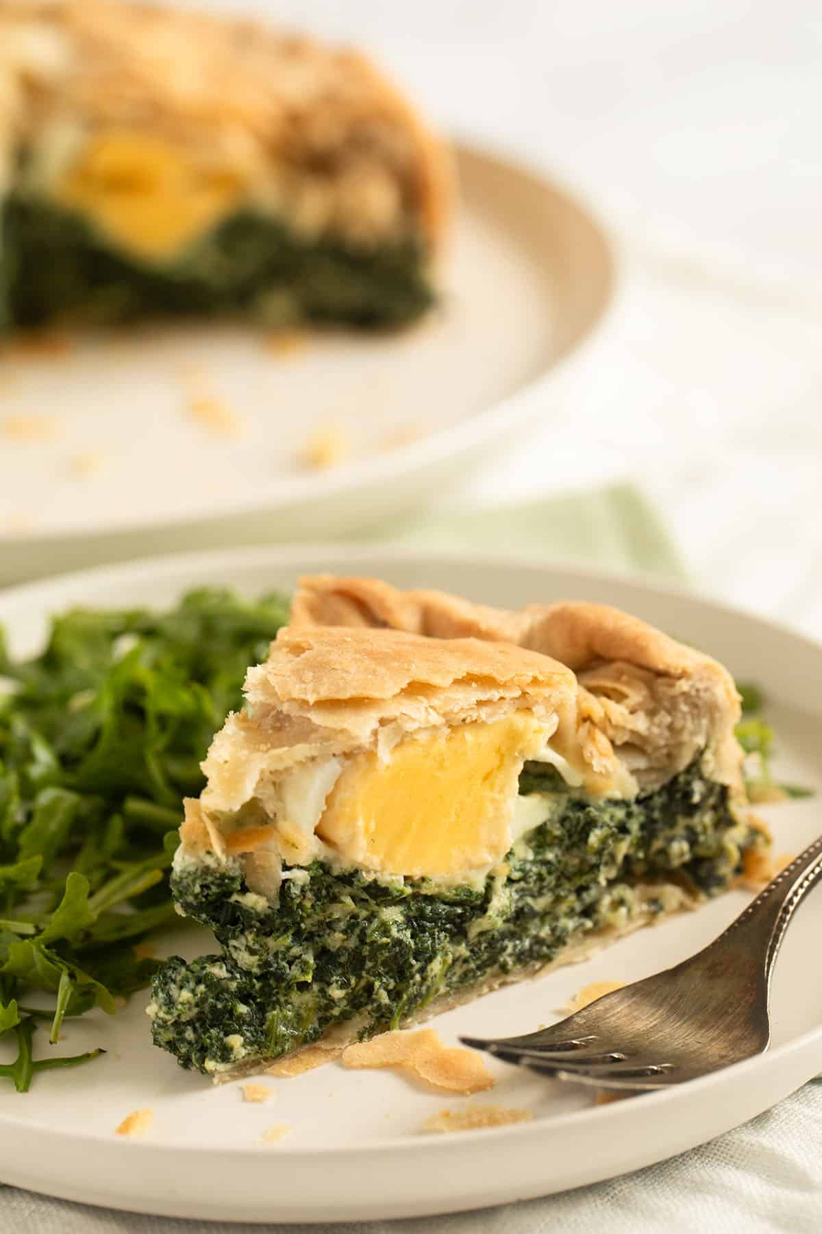 italian spinach pie sliced on a plate and served with arugula salad.