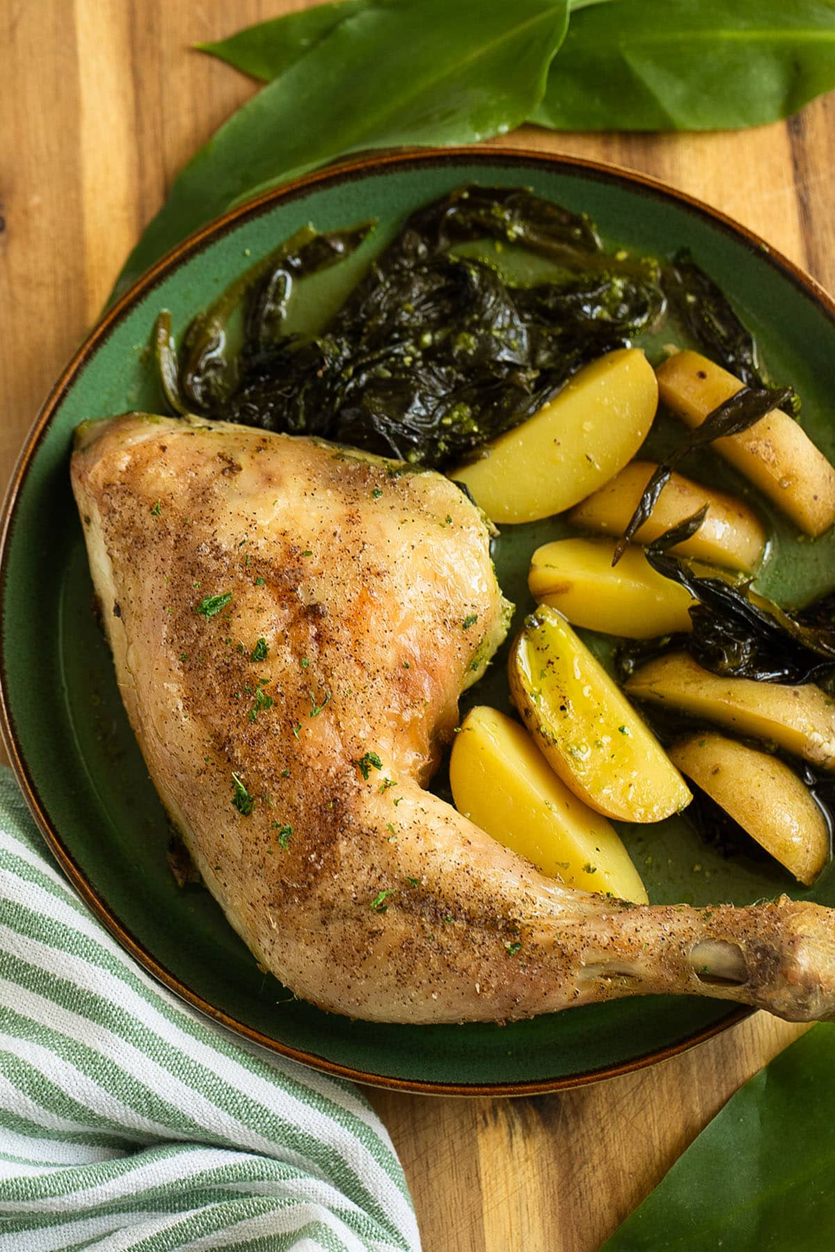 one chicken quarter with potatoes and cooked wild garlic on a plate.