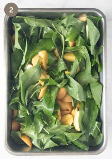 uncooked potatoes and wild garlic leaves in a roasting tin before cooking.