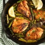 four pieces of golden chicken breasts with asparagus and lemon slices in a skillet.