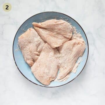 four floured and seasoned chicken breasts on a plate.