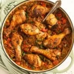 chicken drumsticks and rice in a large dutch oven with a spoon in it.