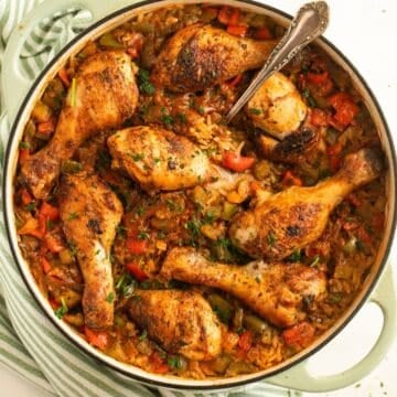 chicken drumsticks and rice in a large dutch oven with a spoon in it.