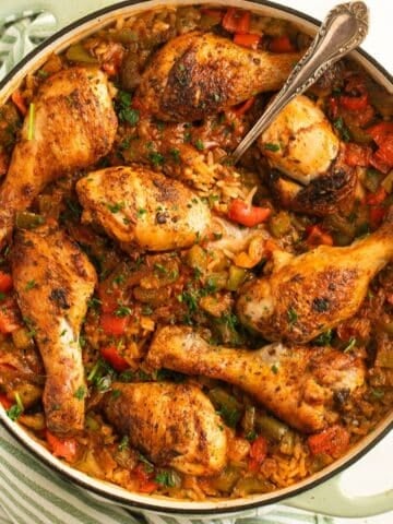 chicken drumsticks and rice in a large dutch oven with a spoon in it.