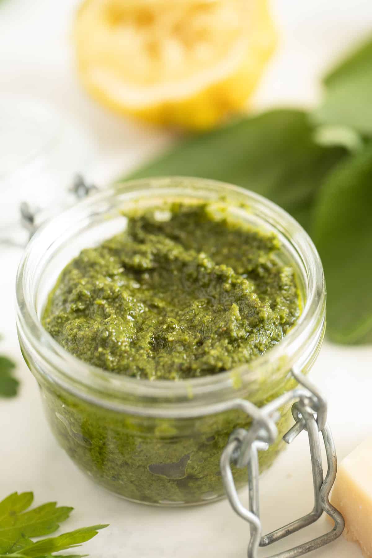 sage pesto in a jar, half a squeezed lemon and sage leaves behind it.