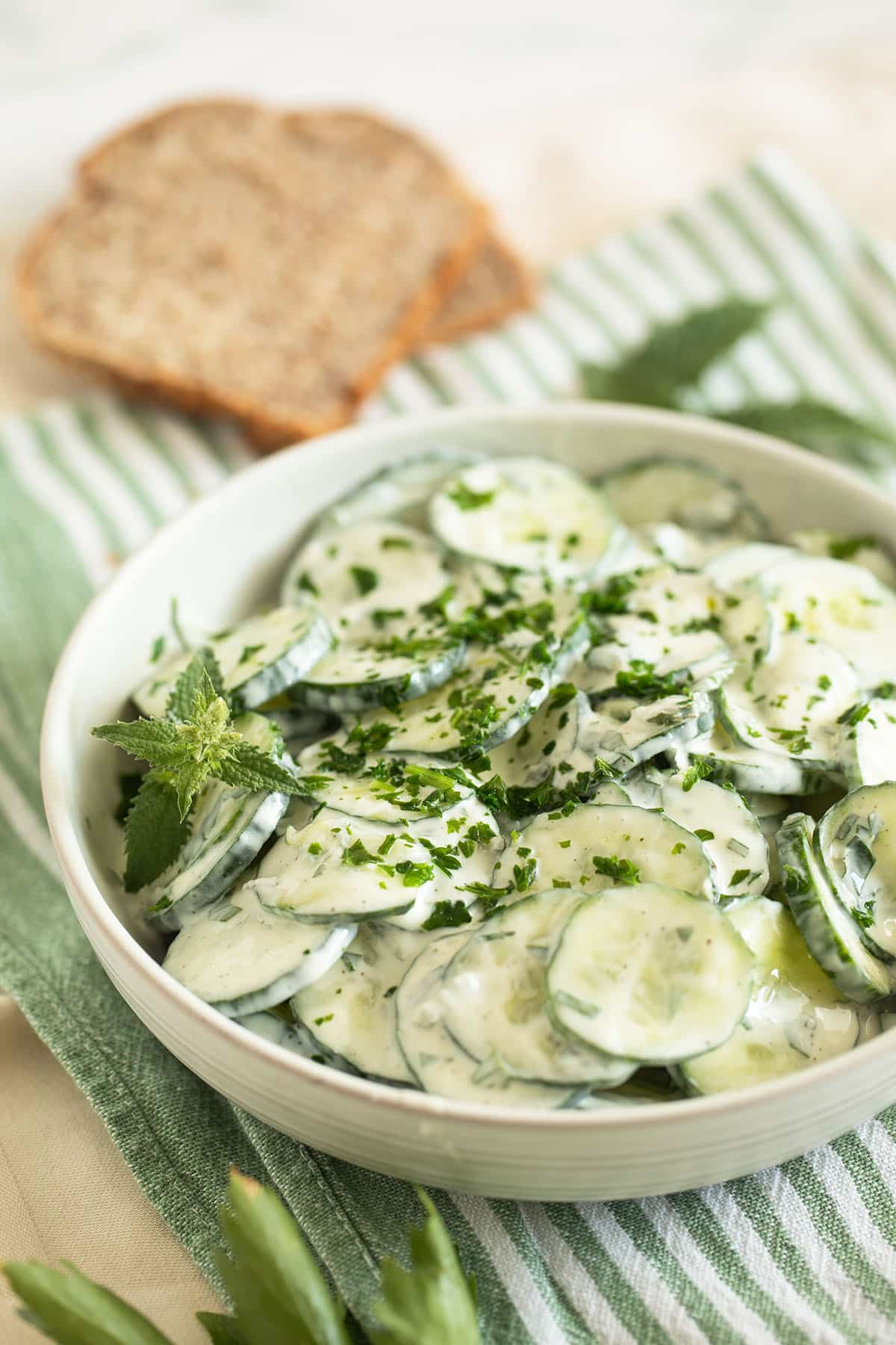 cucumber salad with yogurt dressing in a bowl and two slices of bread behind it.