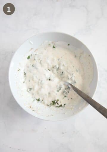 mixing yogurt dressing with chopped mint and parsley in a bowl using a spoon.