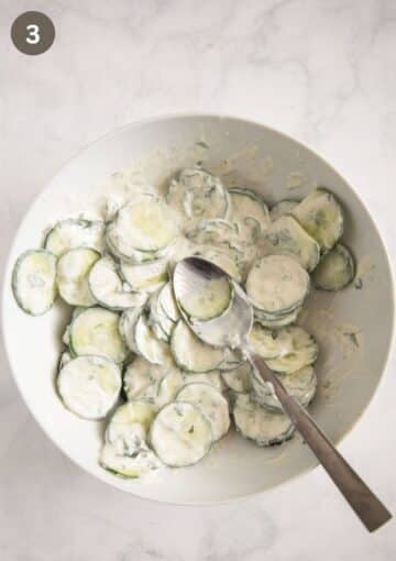 mixing cucumber slices with yogurt dressing in a bowl with a spoon.