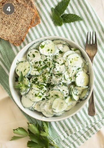 salad with cucumbers, yogurt dressing, mint and parsley, some fresh herbs, bread slices and a fork around it.