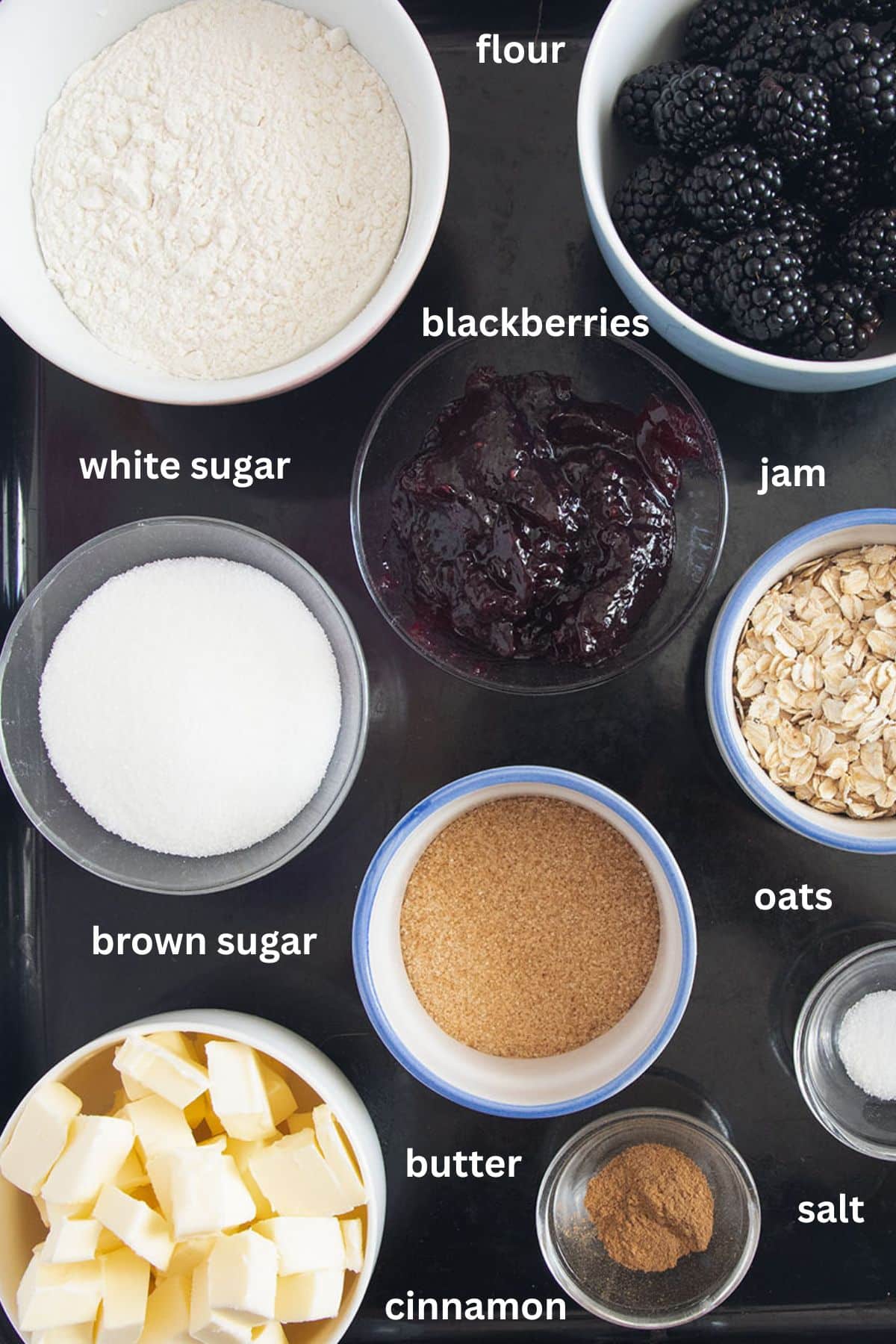 labeled ingredients for making crumble bars with fresh blackberries, oats, butter, flour, sugar, and jam.