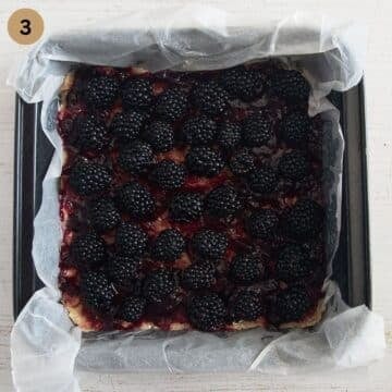 topping bars dough with jam and fresh blackberrie in a baking dish lined with parchment paper.