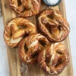 many german pretzels sprinkled with coarse salt on a wooden cutting board.