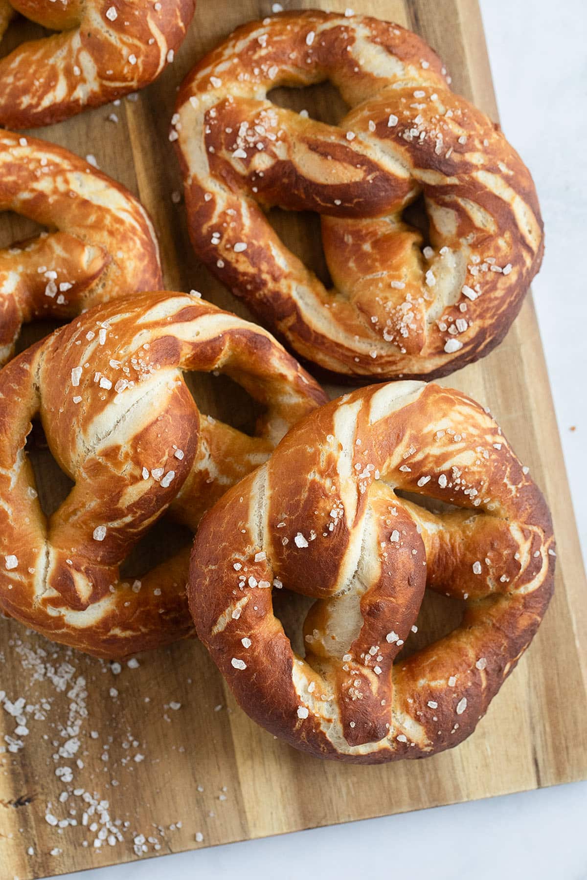 many brown pretzels sprinkled with salt on a cutting board.