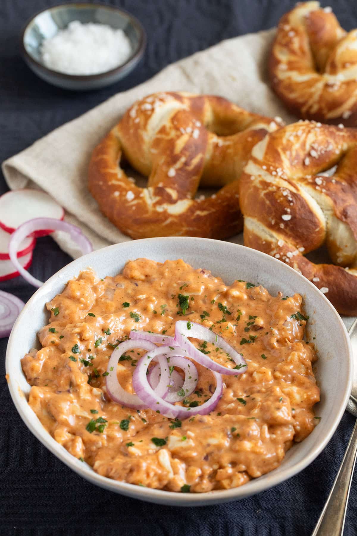a bowl with homemade obatzda and three fresh pretzels behind it.
