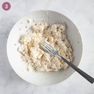 mashing camembert with cream cheese and onions with a fork in a bowl.