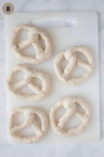 five shaped raw pretzels on a cutting board.