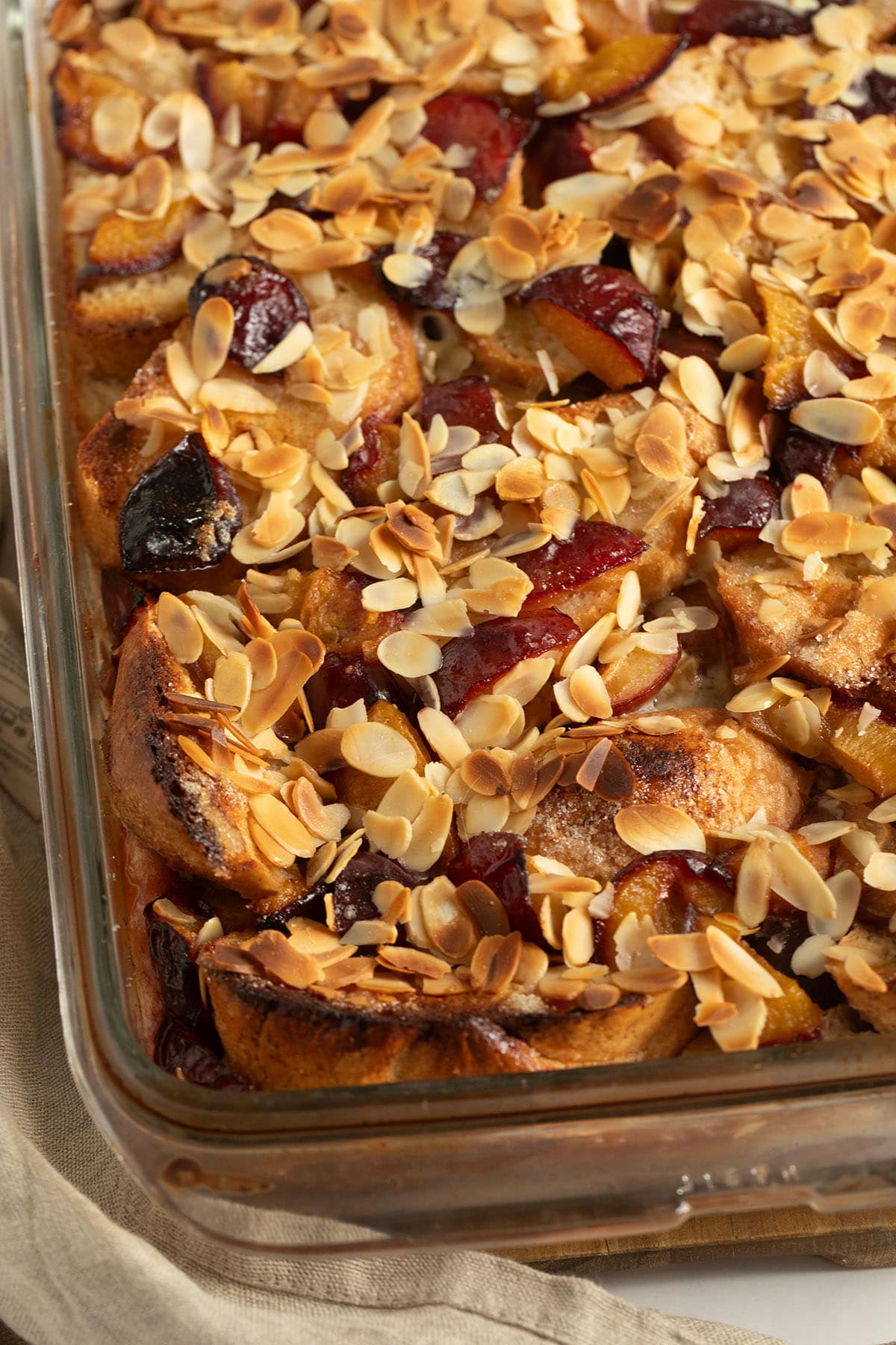 golden baked bread and plum pudding topped with sliced almonds in a baking dish.